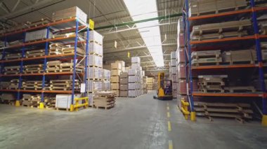 Portakallı bir elektrik istifçisi stoklarında mallarla rafların arasında gidiyor. Şirkette iş akışı.