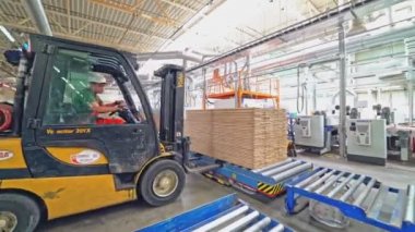 Bir elektrik yükleyicisi metal palete, müşterinin siparişinin altına bir yığın parke levha koyar..