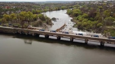 Şehrin dışındaki nehir kıyısında yeşil ağaçlardan ve binalardan oluşan muhteşem bir manzaranın arka planında su arıtma için inşa edilmiş büyük bir köprü var. Yakın plan. Hava görünümü.