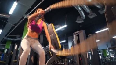Spor merkezinde halatlarla yoğun egzersizler yapan genç bir kadın. Jimnastik salonundaki ince bir kızın fiziksel egzersizleri. Yakın plan.