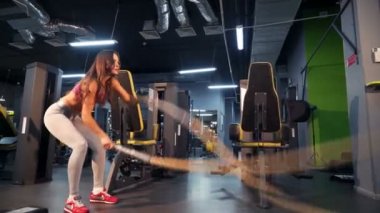 Kaslı fitness kadını yeni bir spor salonunun arka planında iki kabloyla trisepsi eğitiyor. Spor salonunda halat çaprazlama kadın egzersizi..