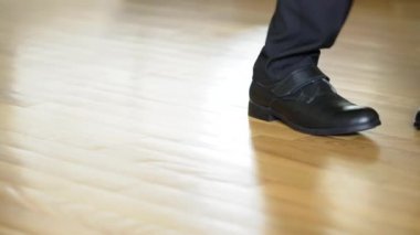 Siyah ayakkabılı bir adamın bacakları kahverengi zeminde dubstep dansı yapıyor. Siyah pantolonlu ayakkabılara ve bacaklara doğru bak..