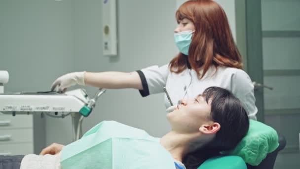 歯医者はブルネットに胃クリニックで歯のホワイトニング手順の後の結果を検査するための鏡を与えます — ストック動画