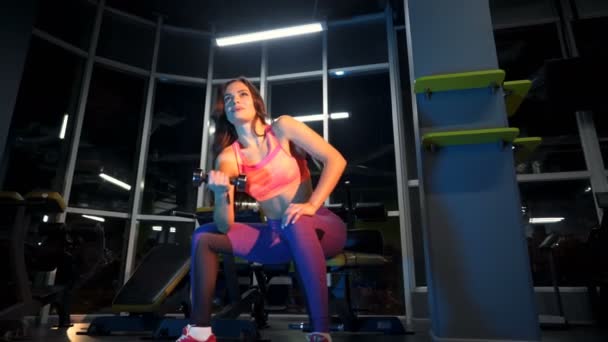 漂亮性感的年轻女人坐在体育馆用金属哑铃做运动 一个肌肉发达的女孩在一个现代化的健身中心训练她的胳膊 — 图库视频影像