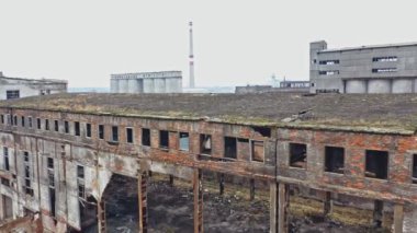 Aynı bölgedeki diğer eski yapıların arka planında hasarlı duvarları olan terk edilmiş eski bir fabrika hangarı. Hava görünümü.