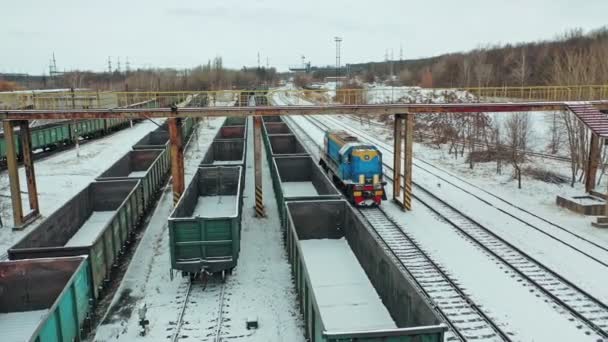 Modrý nákladní vlak přijíždí na místo určení uprostřed velkého množství kontejnerů v zimním dni. Letecký pohled.