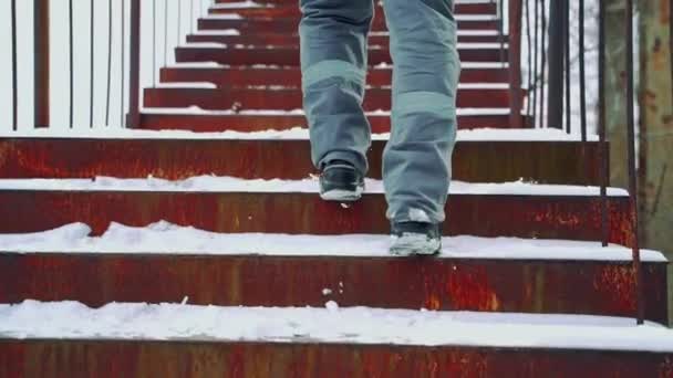 冬天的时候 一个穿着灰色裤子 浅浅的水平条纹和黑色靴子的工人正在街上爬楼梯 腿的特写 — 图库视频影像