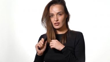 Uzun saçlı düşünceli bir kadın düz ve paralel olarak beyaz bir arka planda saçını tarıyor. Yakın plan..