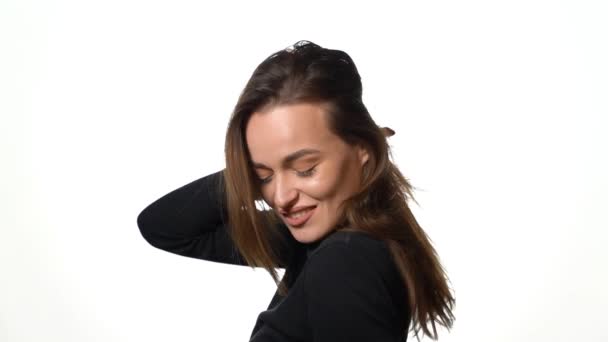 一个穿着黑色套头衫的漂亮模特在工作室的白色背景上翘起她的头发 微笑着 后续行动 — 图库视频影像