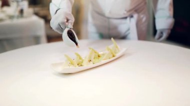 Farklı peynir türlerinin lezzetli aperatifleri beyaz bir tabağa özel kırmızı sos ile dökülür. Aşçı erkek peynirin üzerine sos döker..