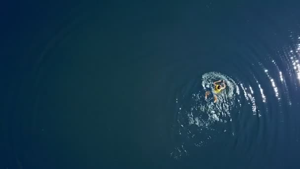 小さな男の子は夏の晴れた日に澄んだ青い水の中で泳いでいます 10代の男の子だけでは 水の背景に黄色の生命ベストの入浴を着て 空中風景 — ストック動画