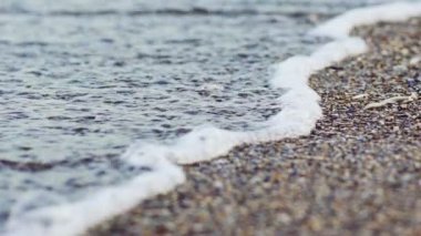 Deniz yüzeyinde, sahilde beyaz köpüklü dalgalar var. Güzel su dalgaları küçük kayalara ve kıyılara çarpıyor. Denizde yaz tatili.