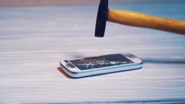木製の背景にハンマーで割れたスマートフォンの画面 ハンマーで壊れた破片と大画面で現代の携帯電話 — ストック動画