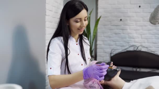 一位长头发的美容师站在顾客的后脑勺上 把洗脸面罩均匀地分布在办公室内部的女人的脸上 — 图库视频影像