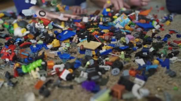 認識できない手は部屋の床に多くのレゴブロックを投げます カーペットの上に横たわる混乱の中で小さなカラフルなレゴのレンガの多く — ストック動画