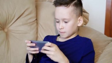 İyi çocuk akıllı telefonuyla oynuyor ve kaybettiğinde sinirleniyor. Kızgın çocuk sandalyede oturuyor ve telefonda oynuyor. Yakın plan.