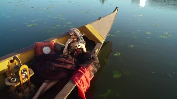 Frau in traditioneller Tracht mit Karnevalsmaske auf einem Boot in Venedig liegend. Attraktive junge sinnliche romantische Frau, die abends in der Gondel schwebt.