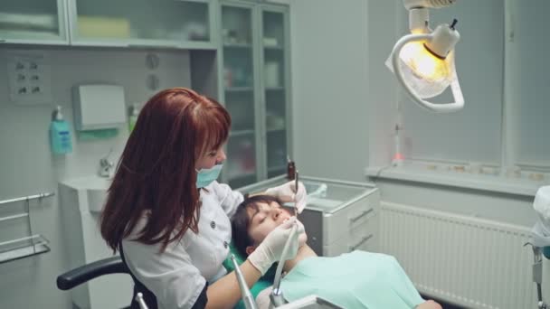 歯科事務所で患者と一緒に働くマスクの専門のスタマトロジスト 歯科医の女性は 光クリニックで特別な機器で前歯を研磨 — ストック動画
