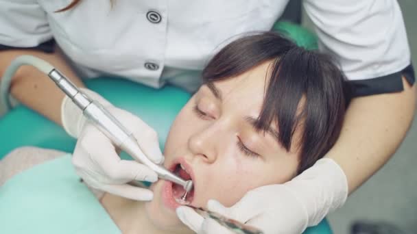 仕事中の白い手袋で患者の顔と胃科医の手のクローズアップ 歯科事務所のサンドブラスト機で歯を洗浄する空気の流れ方法 — ストック動画