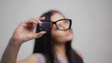 Güzel bir kadın soldan sağa şık gözlükler takar ve onları bulanık bir arka plan ile takar. Koyu saçlı bir kadının elinde şık gözlükler. Yakın plan.