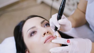 Kalıcı dudak makyajı prosedüründe kanepede uzanmış tatlı bir esmer. Dövme sanatçısı kalemle özel bir pigment uygular. Yakın plan..