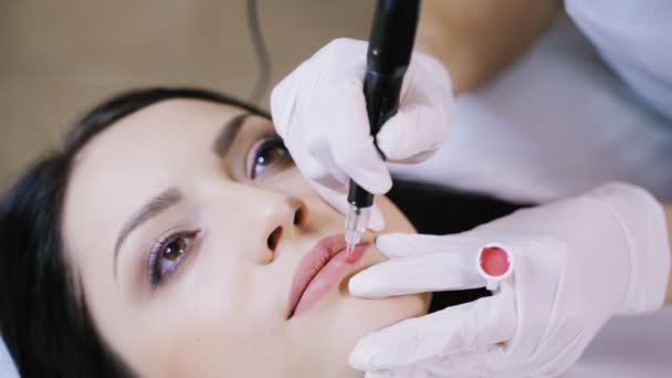 美容師はプロの永久的な化粧機を使用して顧客の唇に優しくピンクの色合いの顔料を適用します — ストック動画