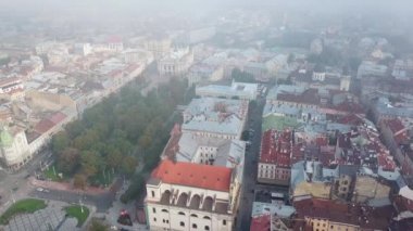 Ukrayna, Lviv 'de eski binaları ve yeşil parkı olan şehir merkezinin güzel manzarası. Lviv 'deki evlerin çatılarının havadan görünüşü. Kamera yukarıdan aşağıya hareket eder.