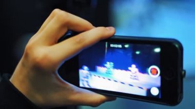 Bir adamın cep telefonunu tutarken ve dans eden robotların fotoğraflarını çekerken görüntüsü.