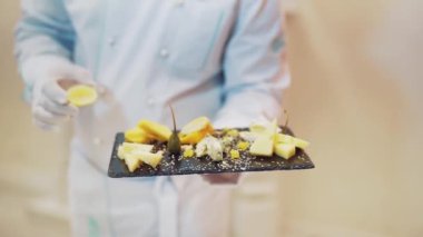 Beyaz elbiseli profesyonel şef tabağı siyah tahtada limonla süslüyor. Restoranda aşçı tarafından sunulan lezzetli peynirin farklı çeşitleri..
