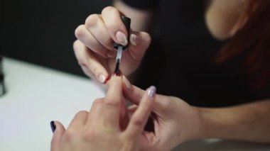 Profesyonel tırnak sanatçısı, kuaförde manikürlü kadınların tırnaklarına oje sürüyor. Usta güzellik merkezinde bir kadına manikür yapıyor. Yakın plan.