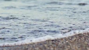 Akşamları çakıl taşlı sahilde akan deniz suyu. Çakıl taşlı arka planda sakin dalgalarla okyanusun kıyısında. Yakın plan..