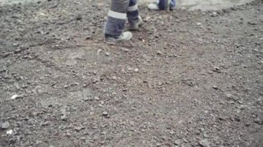 Koruyucu üniformalı işçiler ve yol boyunca kürekli botlar. Bir grup işçi caddede yeni asfalt yapmak için zemin hazırlıyor. Yakın plan.