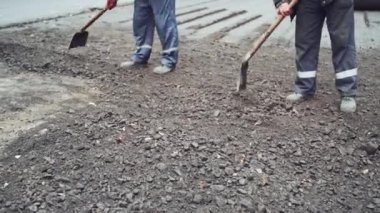Sokak tamiri sırasında ellerinde kürekle üniformalı işçiler. Sokak yeniden ortaya çıkıyor. Taze asfalt yapısı. Yakın plan.