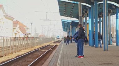 Tren peronunda tren bekleyen iki genç var. Spor elbiseli genç adamlar bir tren istasyonunda birbirleriyle konuşuyorlar..