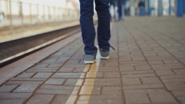 Küçük çocuk tren istasyonunda duruyor ve yolcu trenini bekliyor. Yalnız çocuk platformda ileri geri gidiyor. Yakın plan.