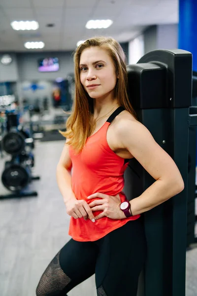 Woman with a beautiful figure in the gym near the boxing equipment. Orange t-shirt.