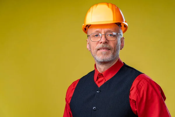 Positive senior engineer in a helmet on a yellow background.