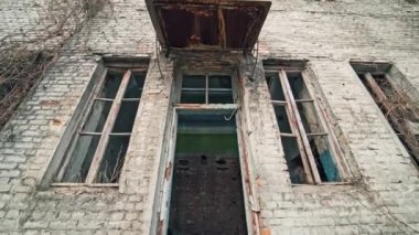 Savaşta camları kırık terk edilmiş bir bina. Dışarıdaki üç katlı tuğla bina hasar görmüş. Kamera geri gider.