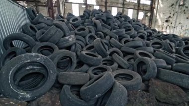 Çatı ve duvarında delikler olan yıkık dökük fabrikada büyük bir araba lastiği yığını. Eski büyük boş binanın içinde yerde bir sürü siyah lastik lastik lastik vardı. Hareket kamerası alttan üste.