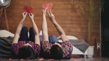 Genç çift yatakta uzanıyor ve elleri ve kırmızı kağıt kalpleriyle oynuyorlar. Kız ve erkek arkadaşı yatak odasında kalpleriyle el ele tutuşuyorlar. Aşk ilişkisi kavramı.