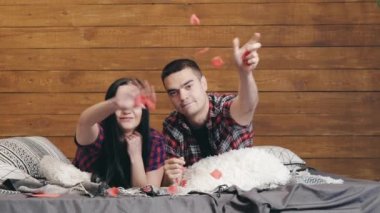 Sevimli sevgili ve sevgili yatakta uzanıp kırmızı kağıt kalpler atıyorlar. Genç bir çiftin evde randevusu var. Sevgililer Günü