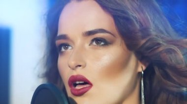 Dalgalı saçlı ve mikrofona yakın uzun küpeli çekici bir şarkıcının yüzü. Stüdyoda şarkı söyleyen güzel bir kadın. Yakın plan.