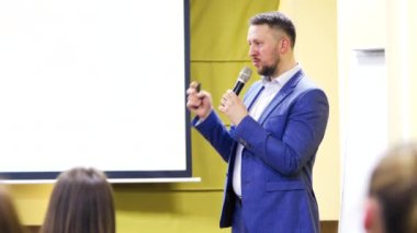Mavi takım elbiseli adam iş konferansında mikrofonla konuşuyor. İdari lider halka açık seminerde konuştu ve el kol hareketi yaptı.