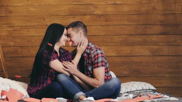 穿着衬衫和牛仔裤的浪漫夫妻快乐地在屋里调情 两个年轻人正坐在床上 试图亲吻对方 恋爱关系概念 — 图库视频影像