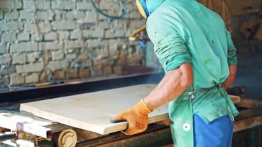 Taştan CNC makinesinde çalışan bir işçi taş fabrikasının levhasını kesiyor. Maskeli ve kulaklıklı erkek işçi, makineye levha takıyor..