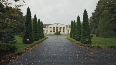 Islak asfalt parktaki büyük ışıklı binaya çıkıyor. Yeşil ağaçlarla dolu güzel bir ara sokak ve sonbaharda huzurlu bir manzara bahçesinde güzel bir mimari..
