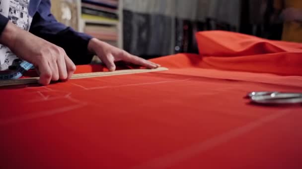 アトリエの赤い布でテーブルで働く女性のテーラー 熟練したシームストレスは 石鹸やチョークと赤い布の定規で線を描くことです — ストック動画
