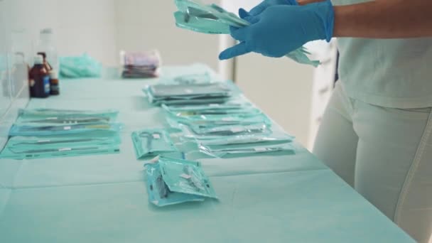 医者か歯医者はテーブルの上に医療機器を置く 歯科治療のためのパック滅菌器のセット 青い手袋の医者の手は歯科クリニックに歯のツールを入れている — ストック動画