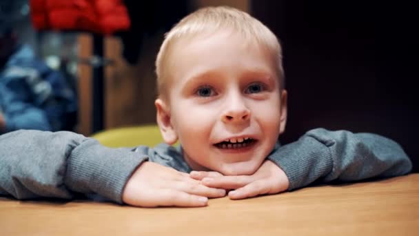 Симпатичный Мальчик Большими Голубыми Глазами Сидит Столом Разговаривает Любопытный Блондин — стоковое видео
