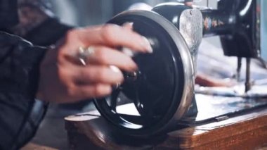 Eski bir dikiş makinesinin metal çarkını döndüren kadın elinin yakın çekimi. Terzi atölyede siyah bir dikiş makinesi üzerinde çalışıyor. El yapımı konsept.